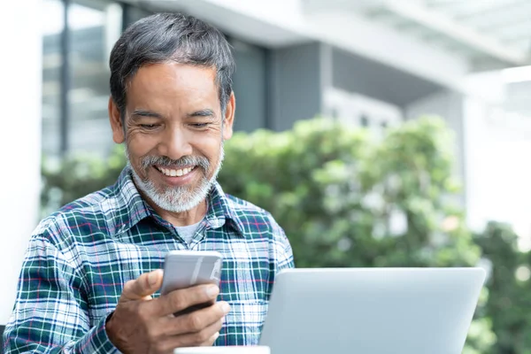 Açık kahve dükkanında internet servis eden akıllı telefon aleti kullanan, beyaz, şık, kısa sakallı mutlu, olgun bir adam. Sosyal medya teknolojisi kullanan gülen yaşlı adam heyecanlanıyor.