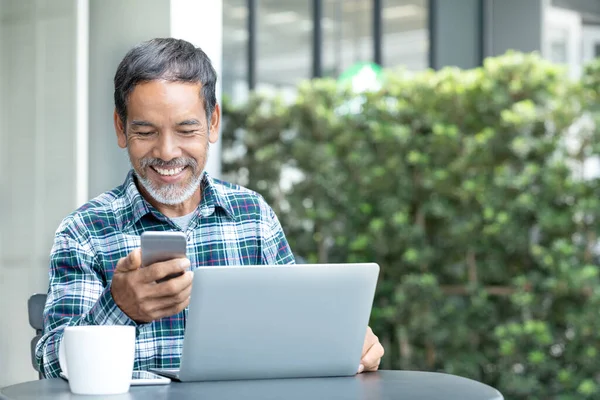 Açık kahve dükkanında internet servis eden akıllı telefon aleti kullanan, beyaz, şık, kısa sakallı mutlu, olgun bir adam. Sosyal medya teknolojisi kullanan gülen yaşlı adam heyecanlanıyor.