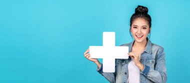 Mutlu Asyalı kadının bayrağı gülümseyen ve elinde tutan artı ya da fotokopi uzayının mavi arka planına işaret koyan. Hoş Asyalı kız günlük kot gömlek giyerek gülümsüyor ve daha fazla konsept için işaret gösteriyor.