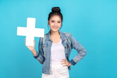 Mutlu Asyalı kadın gülümsüyor ve mavi arka planda artı ya da ekleme işareti gösteriyor. Hoş Asyalı kız günlük kot gömlek giyerek gülümsüyor ve daha fazla ve daha fazla fayda için işaret gösteriyor.