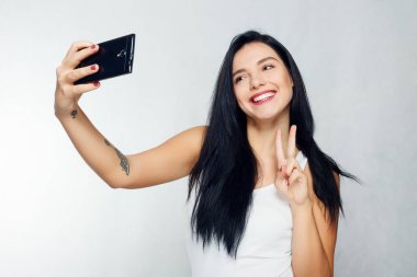Selfie zaman. Genç gülümseyen sarı saçlı Bayan selfie gri arka plan üzerinde yapıyor