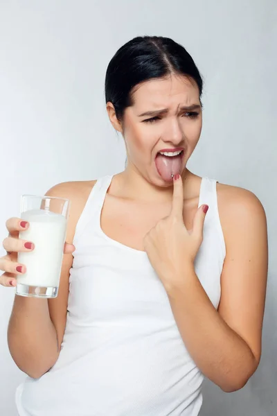 Expressão de uma menina morena segurando um copo de leite, kefir, ryazhenka, produtos lácteos e não gosta de bebê-lo — Fotografia de Stock
