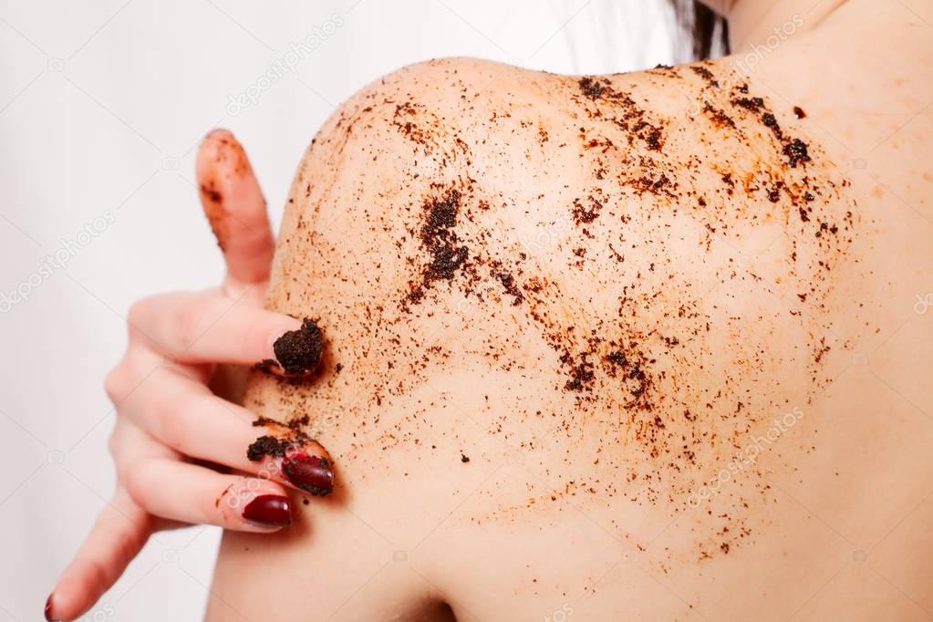 Brunette woman cleans the skin of the body coffee scrub