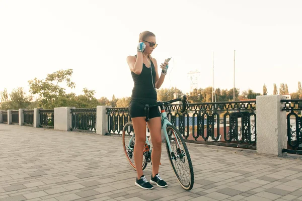 Красивая девушка с велосипедом, телефоном и наушниками — стоковое фото