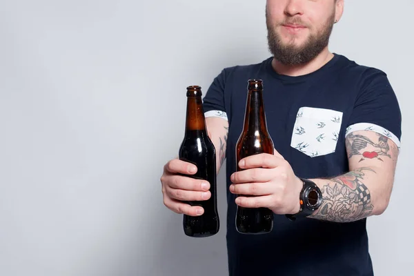 Brutal barbudo macho con brazo tatuado bebe una cerveza de una botella . —  Fotos de Stock
