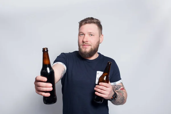 Brutal barbudo macho con brazo tatuado bebe una cerveza de una botella . —  Fotos de Stock