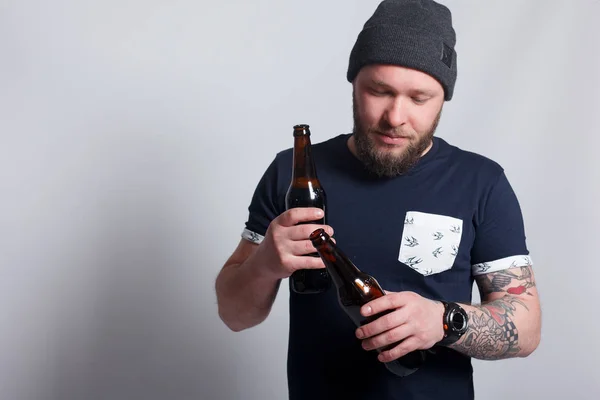Βάναυση γενειοφόρος άνδρας με τατουάζ βραχίονα μια μπύρα ποτά από ένα μπουκάλι. — Φωτογραφία Αρχείου