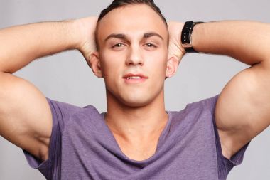 Gri arka plandaki yakışıklı genç adam kameraya bakıyor.