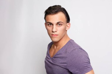 Gri arka plandaki yakışıklı genç adam kameraya bakıyor.