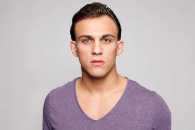 Gri arka plandaki yakışıklı genç adam kameraya bakıyor.