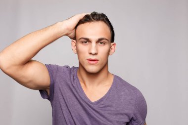 Gri arka plandaki yakışıklı genç adam kameraya bakıyor.