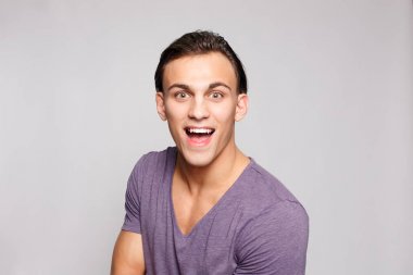 Gri arka plandaki yakışıklı genç adam kameraya bakıyor.