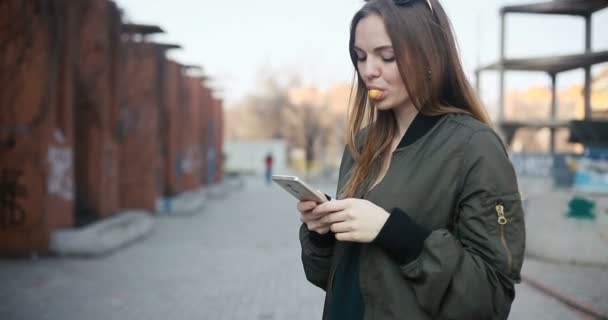 歯科医とライフ スタイル コンセプト 屋外のポートレート スタイリッシュな服チューインガムの若い魅力的な女性の笑顔とカメラを探しています 風船ガムを吹いて内気な少女の肖像画 — ストック動画