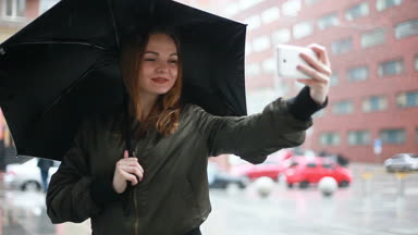 sezon, hava durumu ve insanlar kavramı - genç esmer kadın şemsiye el onstreet ile yağmurlu günde durumda. kadın görüşmeler telefon, Selfie, bir ileti, kadın bak cep telefonu yazıyor mu