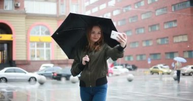 sezon, hava durumu ve insanlar kavramı - genç esmer kadın şemsiye el onstreet ile yağmurlu günde durumda. kadın görüşmeler telefon, Selfie, bir ileti, kadın bak cep telefonu yazıyor mu
