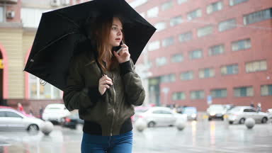 sezon, hava durumu ve insanlar kavramı - genç esmer kadın şemsiye el onstreet ile yağmurlu günde durumda. kadın görüşmeler telefon, Selfie, bir ileti, kadın bak cep telefonu yazıyor mu