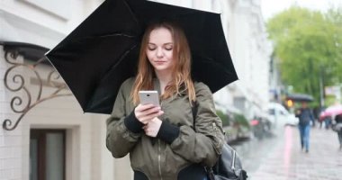 sezon, hava durumu ve insanlar kavramı - genç esmer kadın şemsiye el onstreet ile yağmurlu günde durumda. kadın görüşmeler telefon, Selfie, bir ileti, kadın bak cep telefonu yazıyor mu