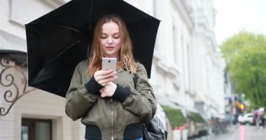sezon, hava durumu ve insanlar kavramı - genç esmer kadın şemsiye el onstreet ile yağmurlu günde durumda. kadın görüşmeler telefon, Selfie, bir ileti, kadın bak cep telefonu yazıyor mu