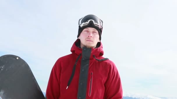ポートレートクローズアップクールなハンサムな男若いスノーボーダー外冬のスキーリゾート探しカメラ陽気な笑顔青い目ヘルメットアクティビティスポーツライフスタイル極端な男性の山スキー人 — ストック動画