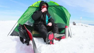 Ayakçı dinleniyor. Kamp sonrası bulutların keyfini çıkarıyor. Dağlarda çadırda oturan bir snowboardcunun portresi. Termostan çay içmek