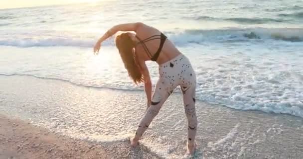 身着紧身衣的年轻女子 日出时分 在海滩上练习瑜伽 瑜伽和健康的生活方式概念 慢动作 — 图库视频影像