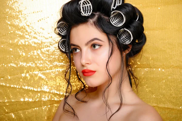 Beautiful girl in hair curlers isolated on gold