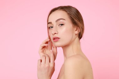 Güzel genç kız pembe arka planda kusursuz tenine dokunuyor..