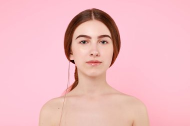 Güzel genç kız pembe arka planda kusursuz tenine dokunuyor..