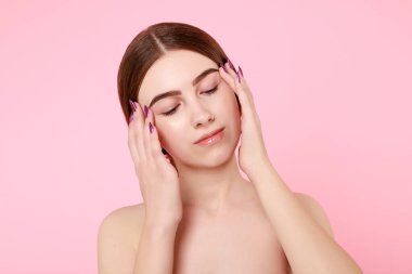 Güzel genç kız pembe arka planda kusursuz tenine dokunuyor..