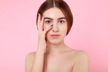 Güzel genç kız pembe arka planda kusursuz tenine dokunuyor..