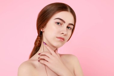 Güzel genç kız pembe arka planda kusursuz tenine dokunuyor..