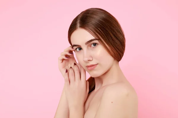 Красива молода дівчина торкається її ідеальної шкіри на рожевому фоні . — стокове фото