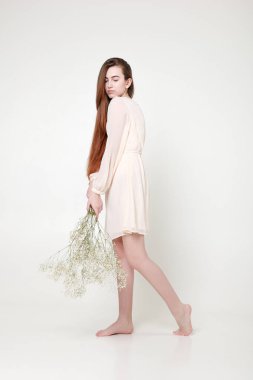 Kıvırcık romantik görünüş, güzel gözler. Beyaz kır çiçekleri ellerinde.