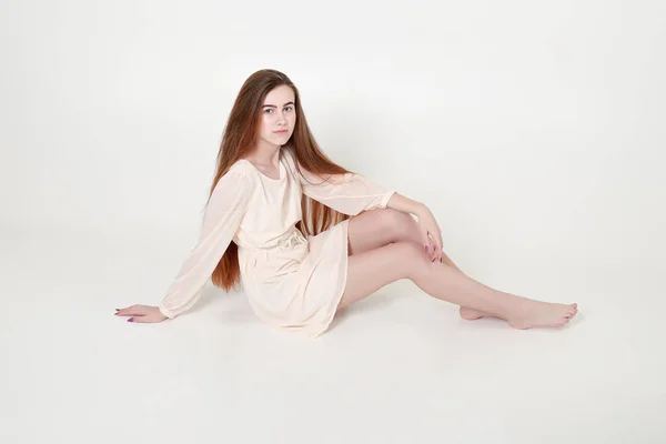 Menina jovem macia bonita em um vestido longo branco e com cabelos longos senta-se — Fotografia de Stock