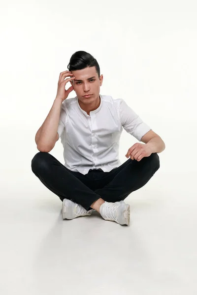 Beau, jeune, homme à la mode est assis sur le sol dans le studio — Photo