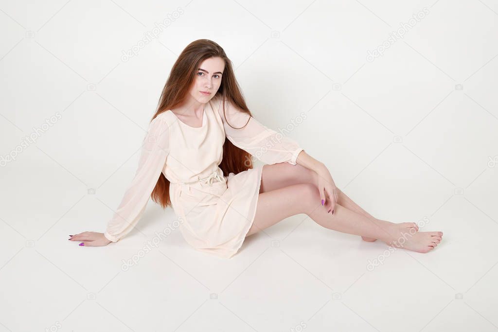 Beautiful tender young girl in a white long dress and with long hair sits