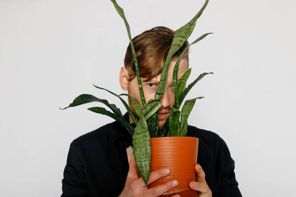 Молодой улыбающийся мужчина держит в руках маленький цветок
