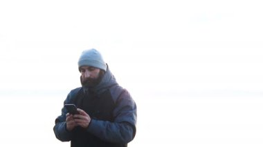 Adam akıllı telefonuyla Sunset 'te karlı vahşi bir arazide fotoğraf çekiyor. Yalnız bir yetişkinin arka planda kalan vahşi deniz manzaralı güzel resimlerine bakması..