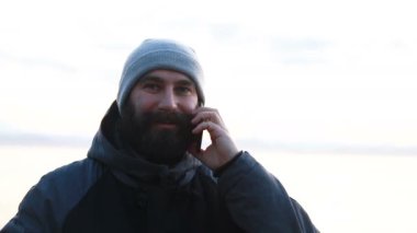 Adam akıllı telefonuyla Sunset 'te karlı vahşi bir arazide fotoğraf çekiyor. Yalnız bir yetişkinin arka planda kalan vahşi deniz manzaralı güzel resimlerine bakması..