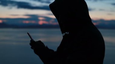 Adam akıllı telefonuyla Sunset 'te karlı vahşi bir arazide fotoğraf çekiyor. Yalnız bir yetişkinin arka planda kalan vahşi deniz manzaralı güzel resimlerine bakması..