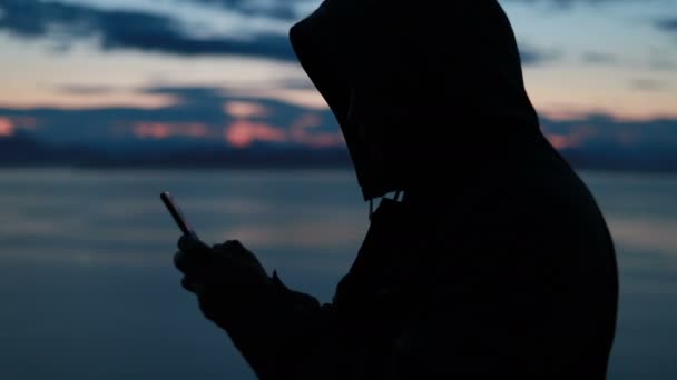 在日落时 人类带着他的智能手机在雪地的野景中拍照 回头看一个孤独的成年人 他正呆在一边 环顾四周 欣赏着野外海滨的美景 — 图库视频影像