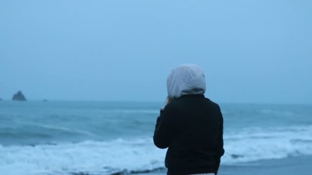 夕阳西下的女人 在冬天看着大海 想着爱情 多云的太平洋 在黑色沙滩上行走的女人 — 图库视频影像