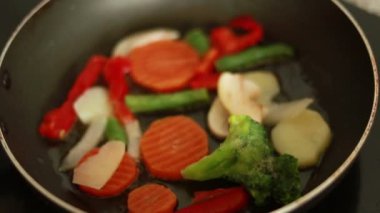 Mutfakta tavada sebze pişiriyorum. Yakın çekim (yavaş çekim). Kızartma tavasında yanan taze sebzeler. Vejetaryen yaşam tarzı, sağlıklı yiyecekler, pişirme süreci. Sebzeler tavada