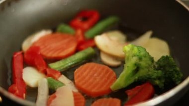 Mutfakta tavada sebze pişiriyorum. Yakın çekim (yavaş çekim). Kızartma tavasında yanan taze sebzeler. Vejetaryen yaşam tarzı, sağlıklı yiyecekler, pişirme süreci. Sebzeler tavada