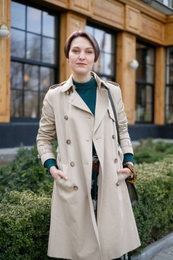 Çekici, şık, kestirme bir kadının portresi, kız açık havada yürüyor. Modern ve kadınsı bir imaj, tarz. Bej pelerinli ve yeşil elbiseli bir kız.