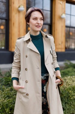 Çekici, şık, kestirme bir kadının portresi, kız açık havada yürüyor. Modern ve kadınsı bir imaj, tarz. Bej pelerinli ve yeşil elbiseli bir kız.