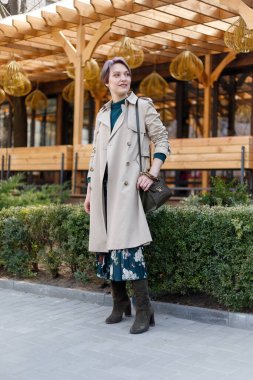 Çekici, şık, kestirme bir kadının portresi, kız açık havada yürüyor. Modern ve kadınsı bir imaj, tarz. Bej pelerinli ve yeşil elbiseli bir kız.