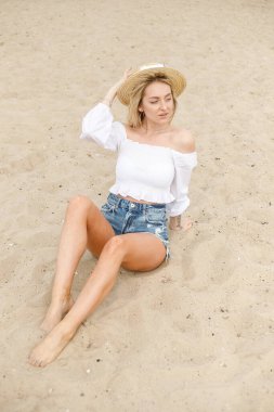 Sarı kıvırcık saçlı inanılmaz bir genç kız rüzgardan gelişiyor, kafasında hasır şapkasıyla denize karşı tatlı tatlı gülümsüyor.