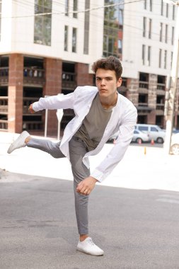 Beyaz gömlekli ve gri pantolonlu şık saç kesimi olan bir erkek model. Modayı takip eden saç stili modern bir iş merkezine yakın. Bir yaz gününde sokakta çekici bir adam..