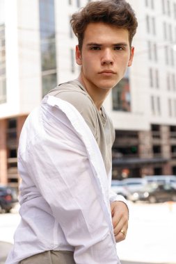 Beyaz gömlekli ve gri pantolonlu şık saç kesimi olan bir erkek model. Modayı takip eden saç stili modern bir iş merkezine yakın. Bir yaz gününde sokakta çekici bir adam..